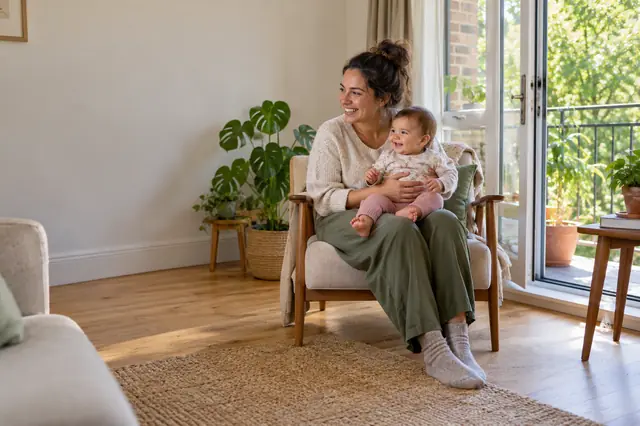 A mother holding her baby in a bright, tidy flat with the balcony door open